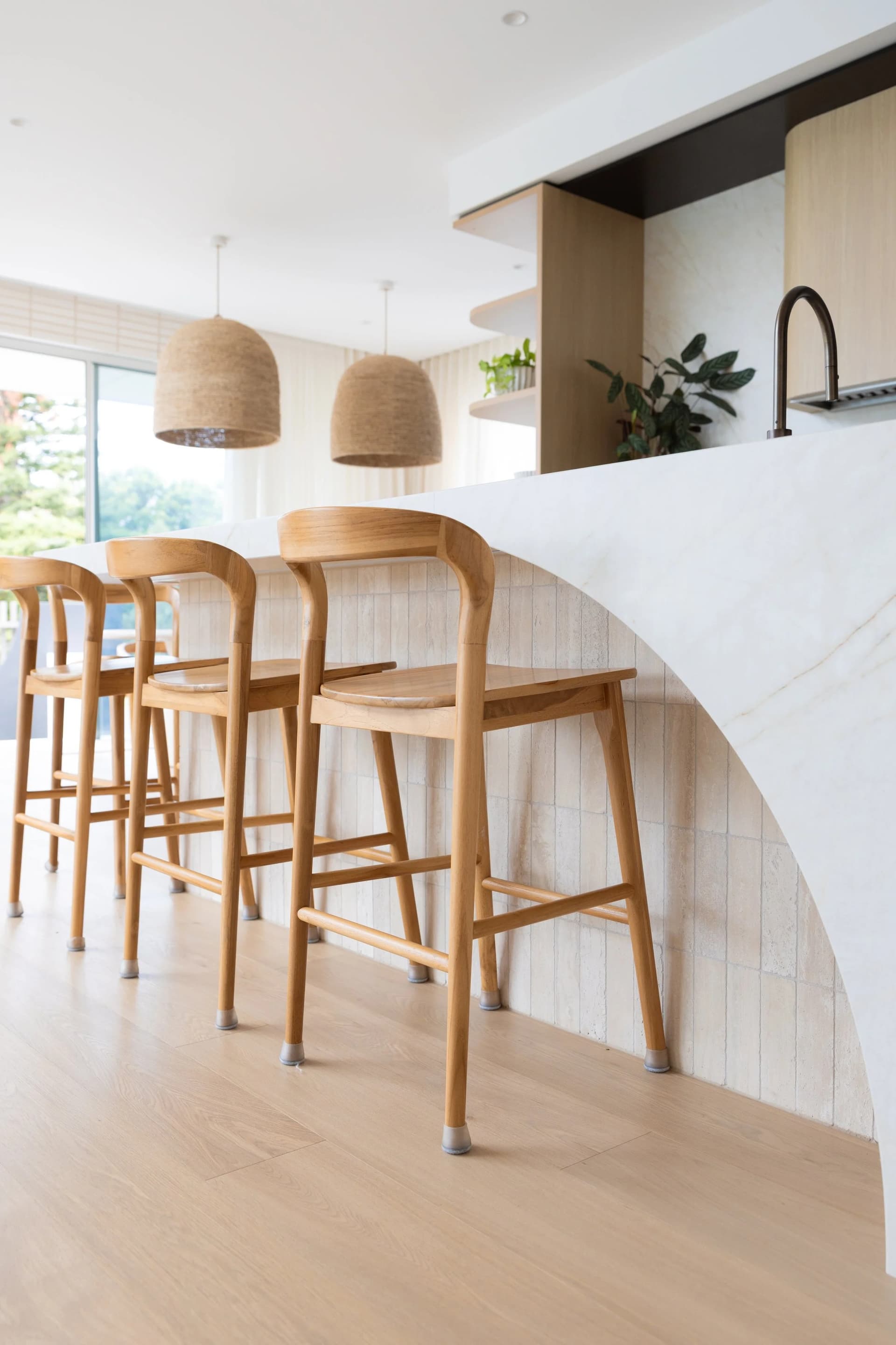 The island's curved travertine return with oak bar stools
