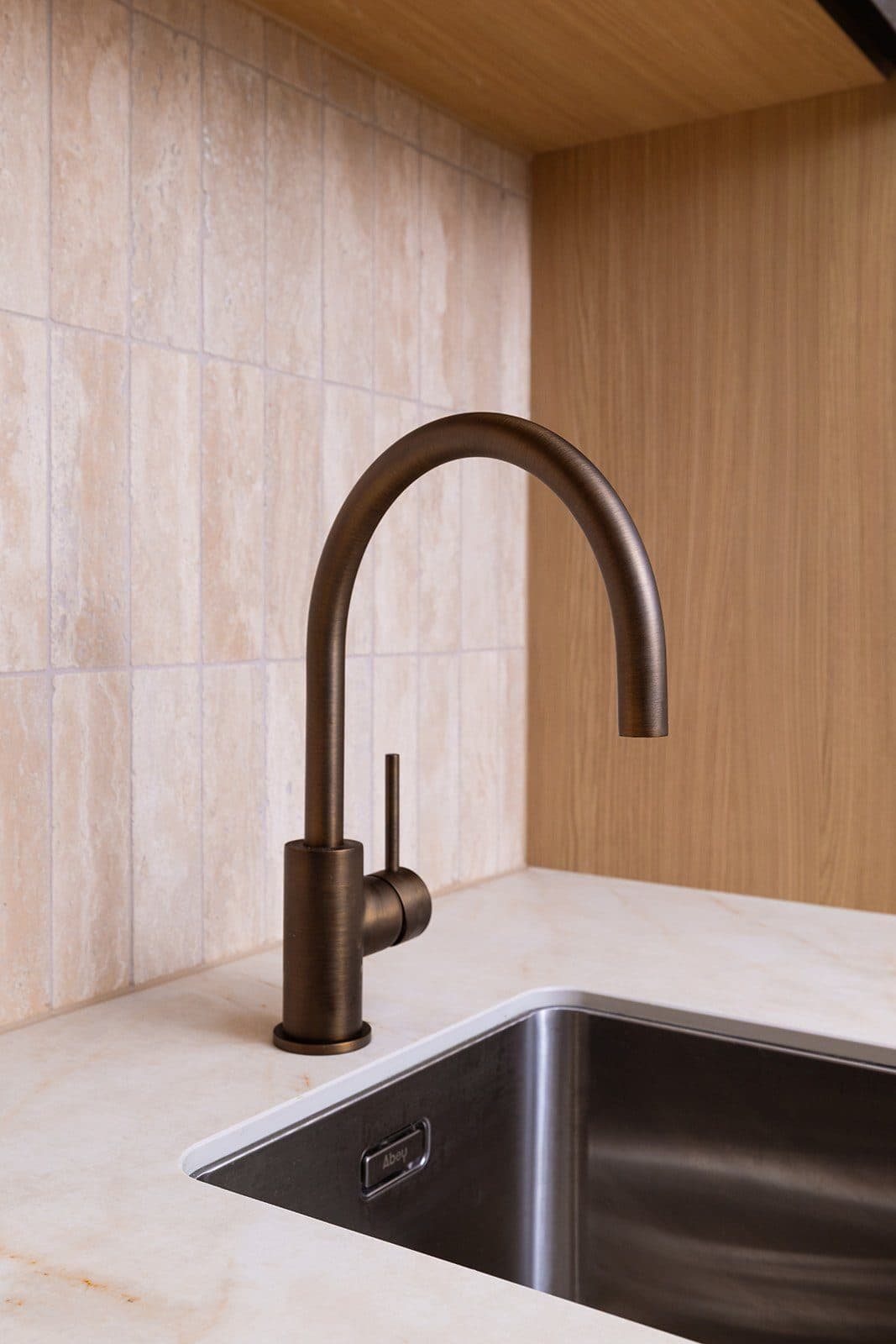 Detail — aged-bronze gooseneck tap over a brushed steel sink