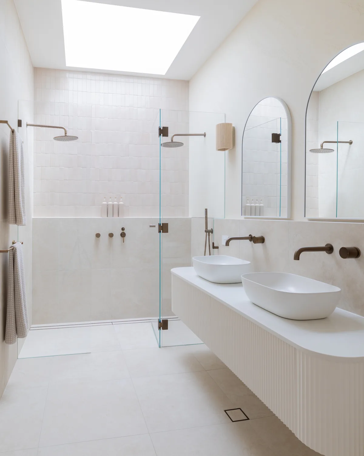 Skylit ensuite at Allard Street — tumbled stone, twin basins and brushed-bronze tapware