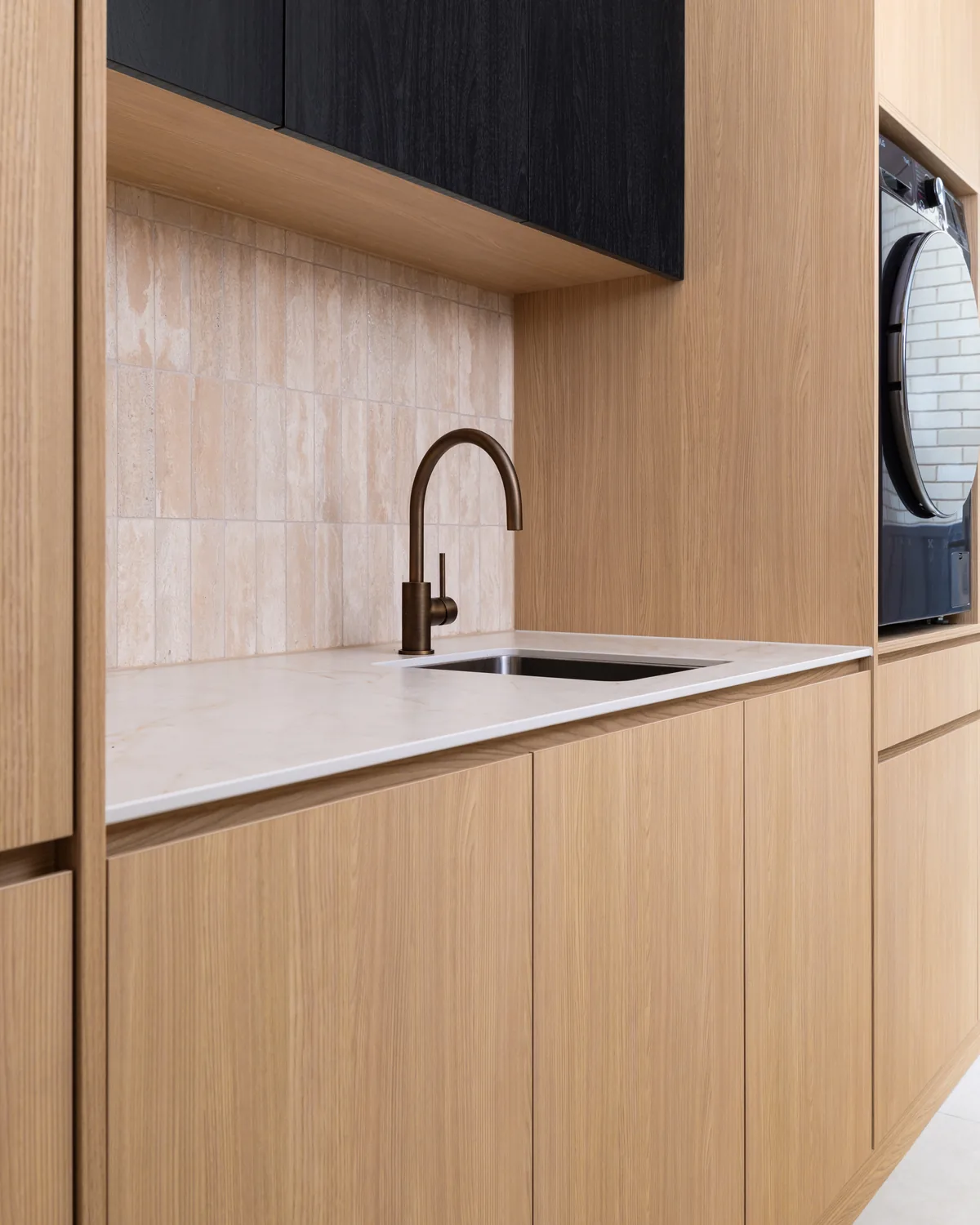 Custom oak laundry joinery with travertine splashback, stone benchtop and aged-brass tapware
